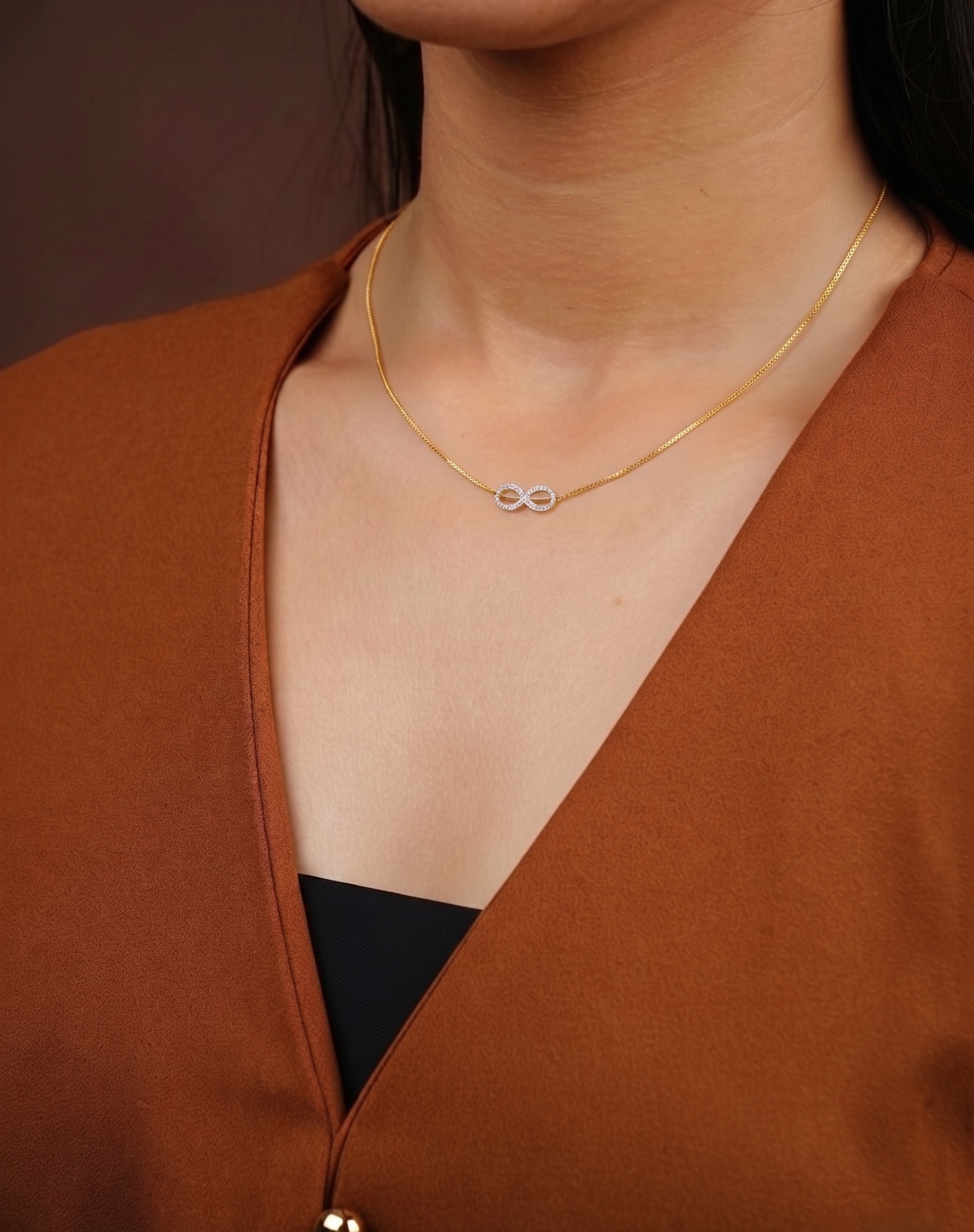Gold necklace with a unique design worn by a person in a brown top.