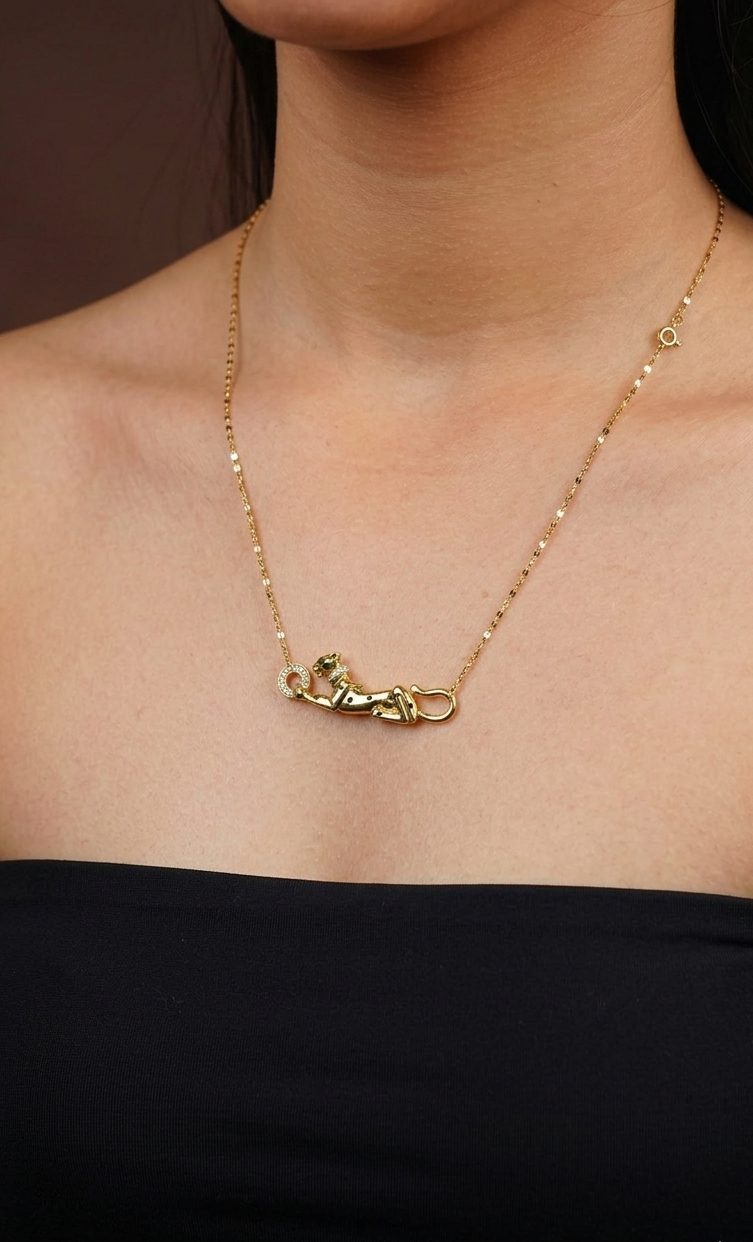 Gold necklace with a pendant on a person wearing a black top against a brown background