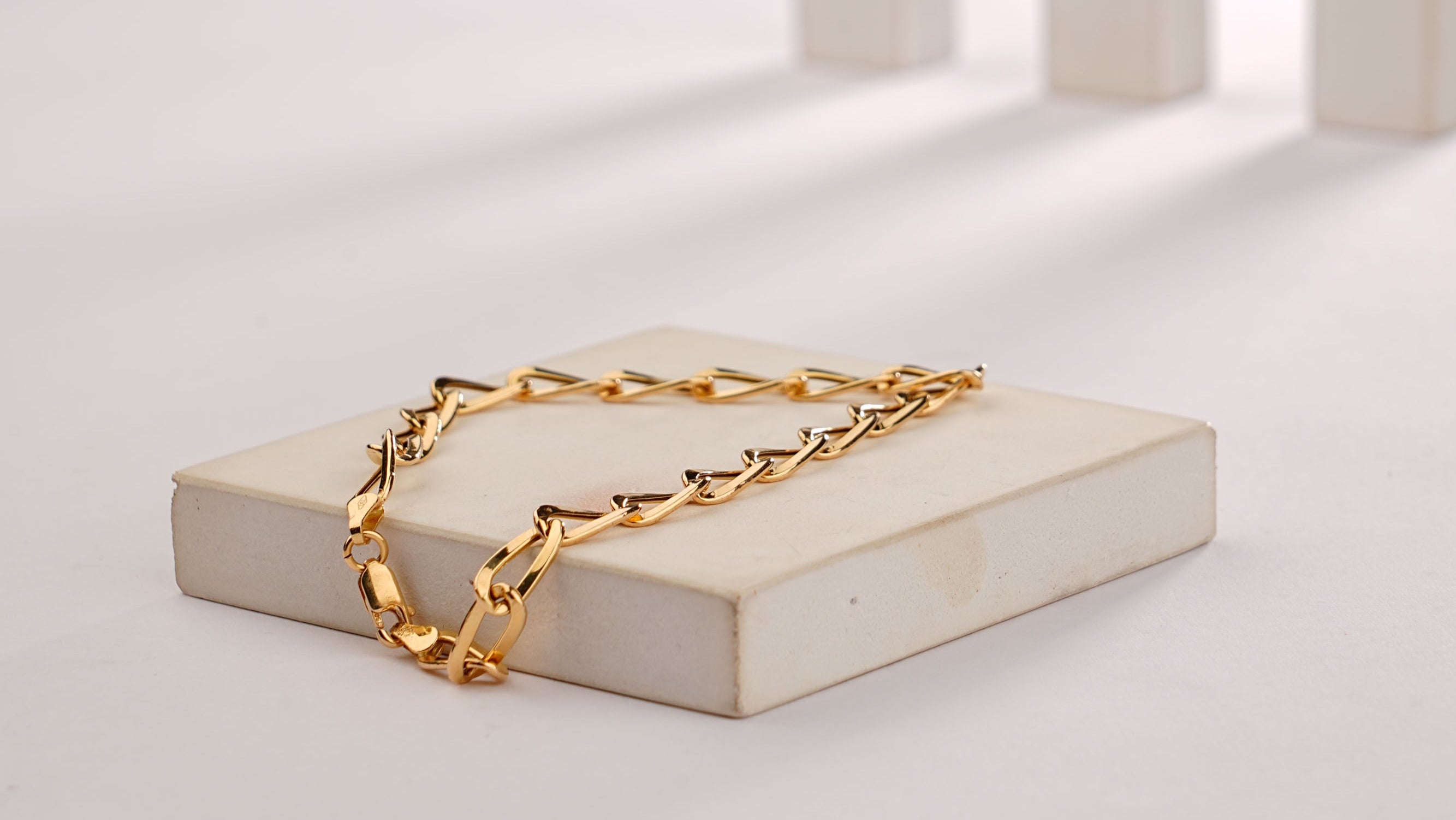 Gold chain bracelet on a white rectangular platform with a gray background