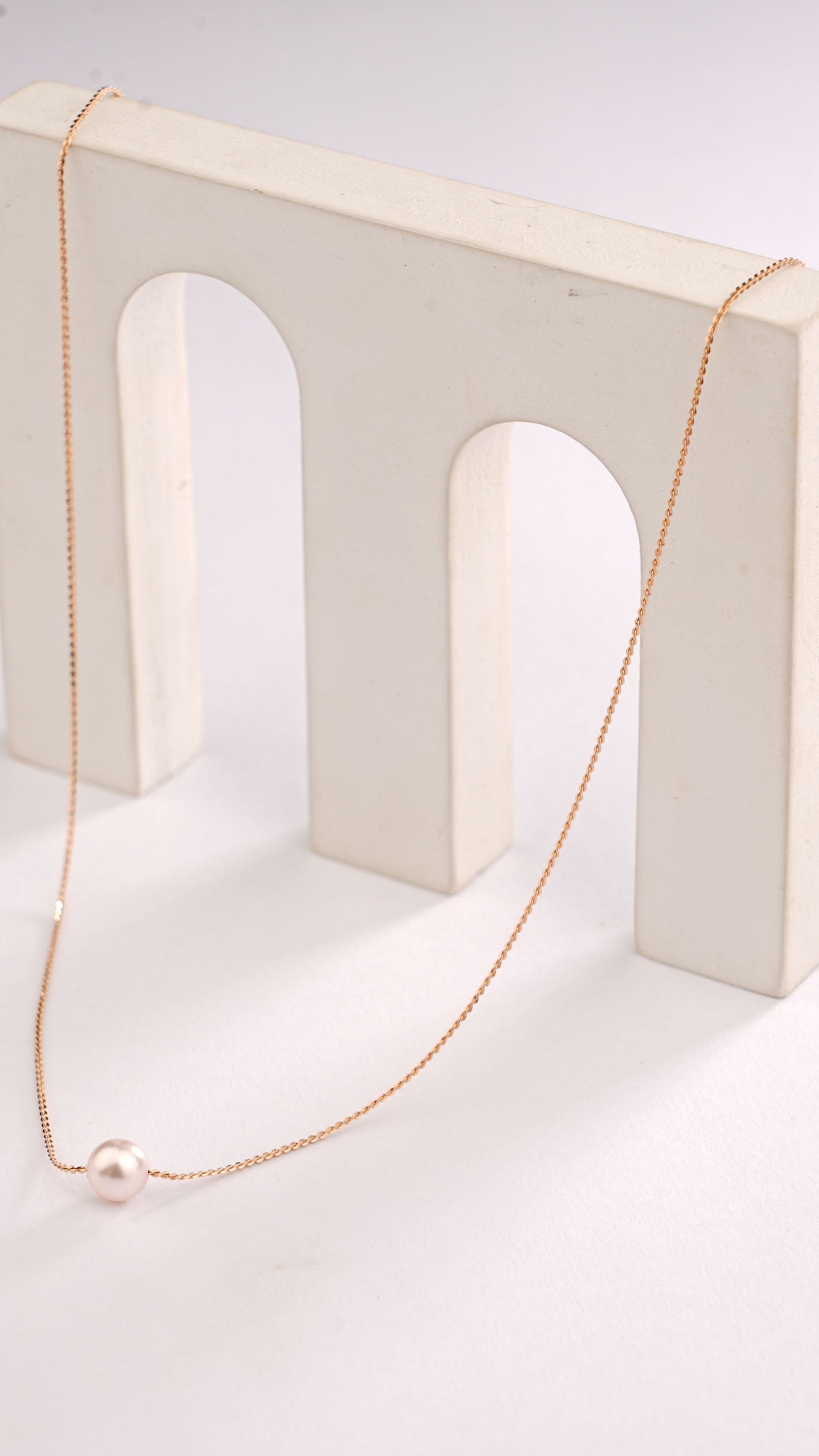 Gold necklace on a white stand against a white background