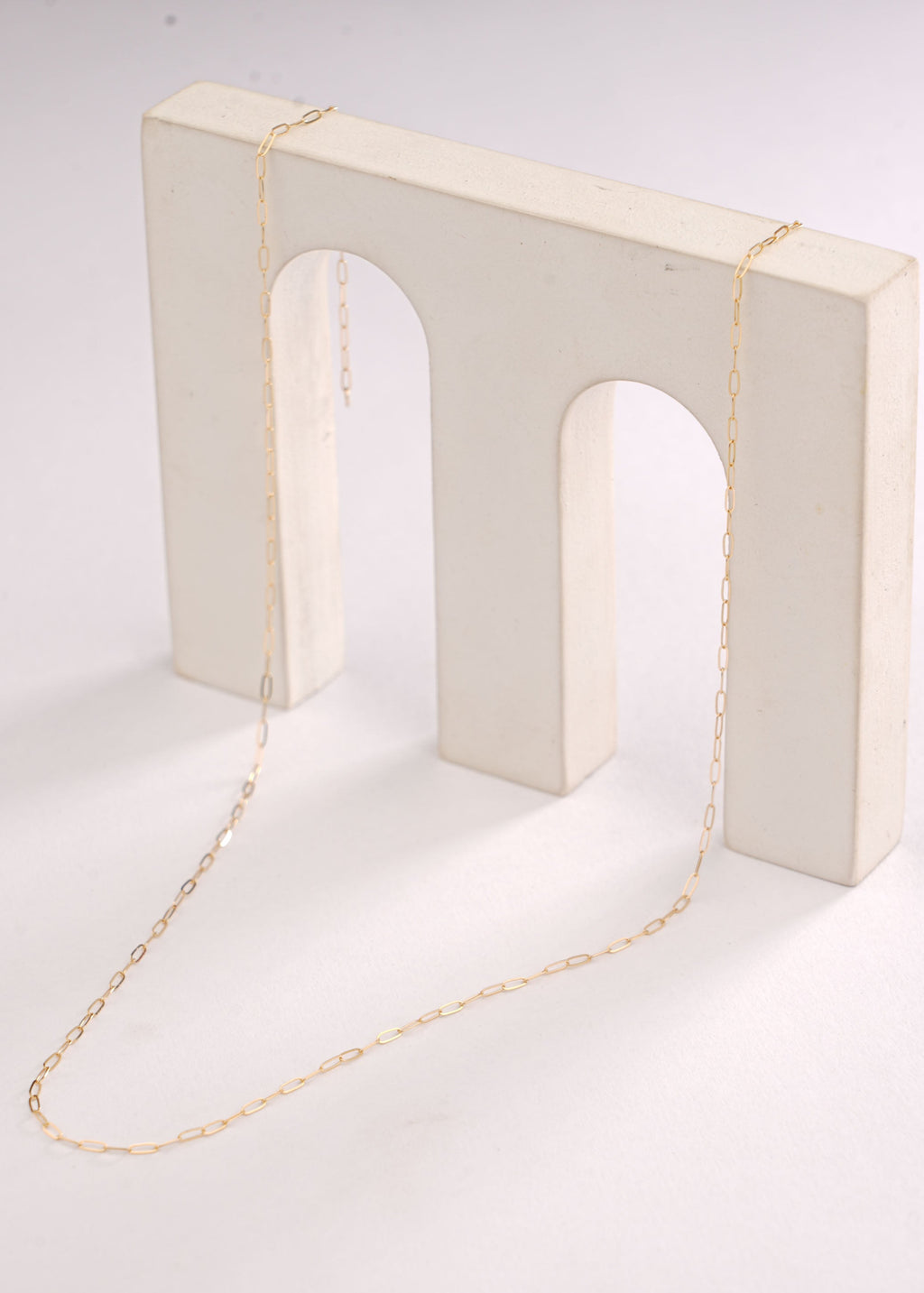 Gold necklace on a white stand with a plain background