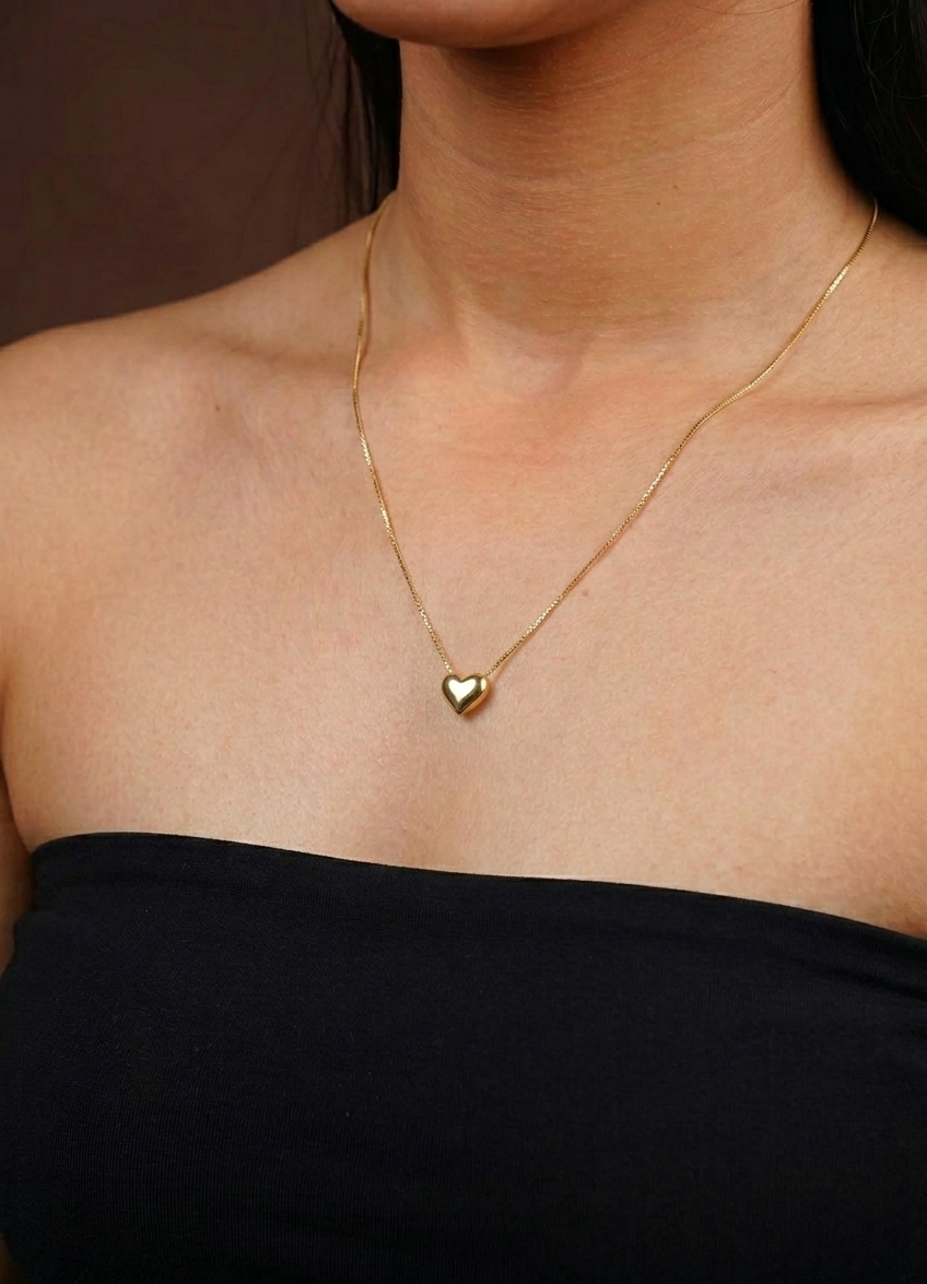 Gold necklace with a heart pendant worn by a person against a neutral background