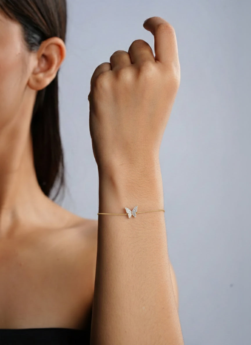 Woman wearing a delicate gold bracelet with a butterfly charm on a neutral background