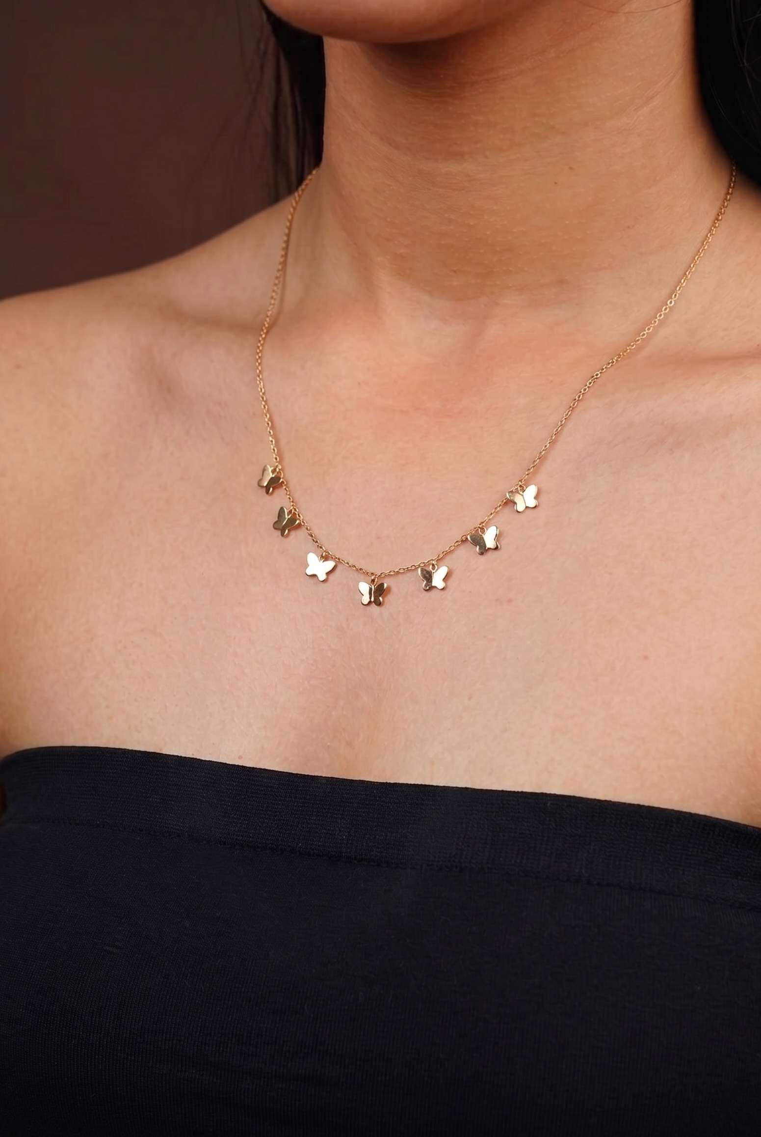 Gold necklace with star-shaped pendants on a person wearing a black strapless top.