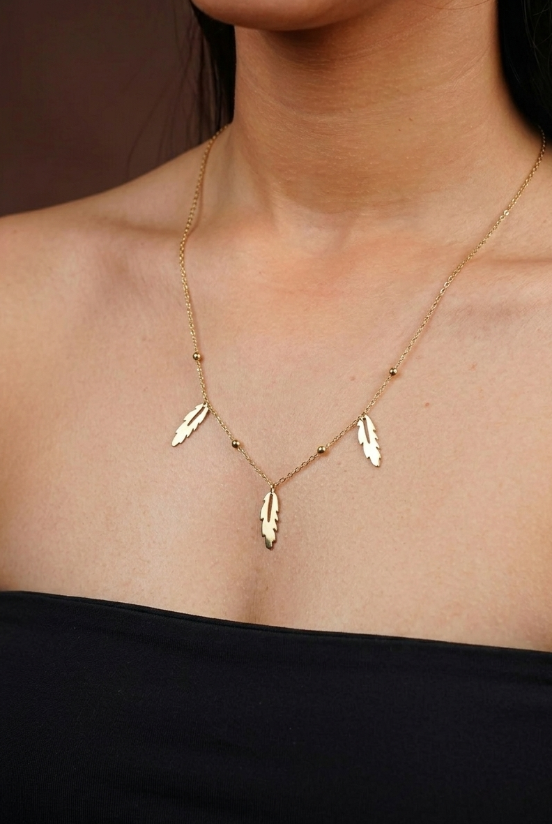 Gold necklace with feather-shaped pendants on a person wearing a black top.