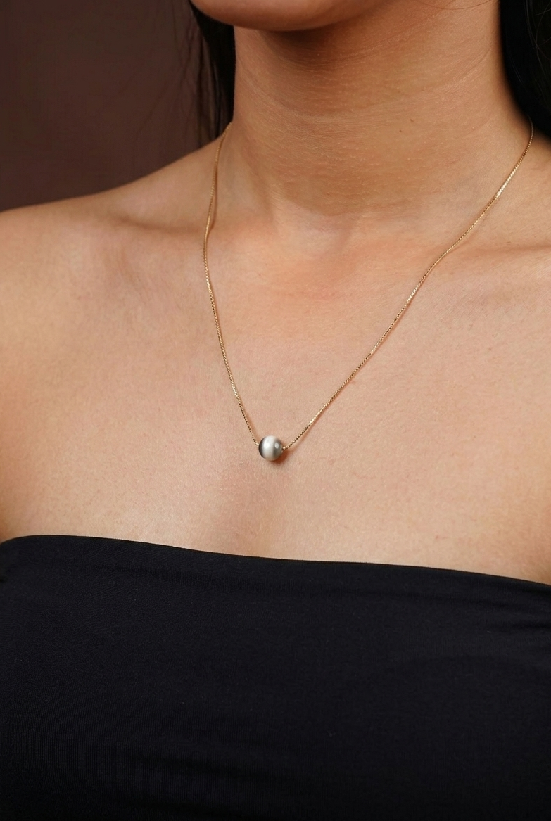 Gold necklace with a pendant on a person wearing a black top against a brown background