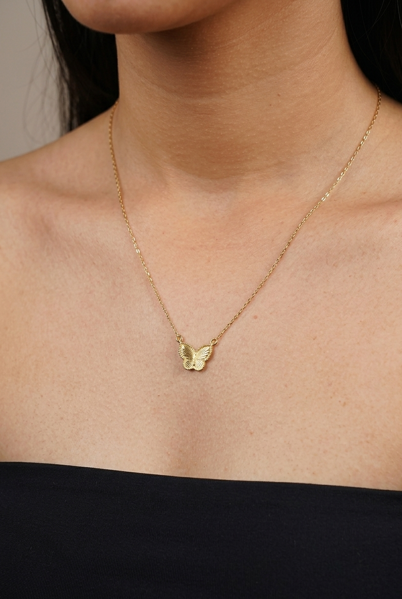 Gold necklace with a butterfly pendant on a person wearing a black top.