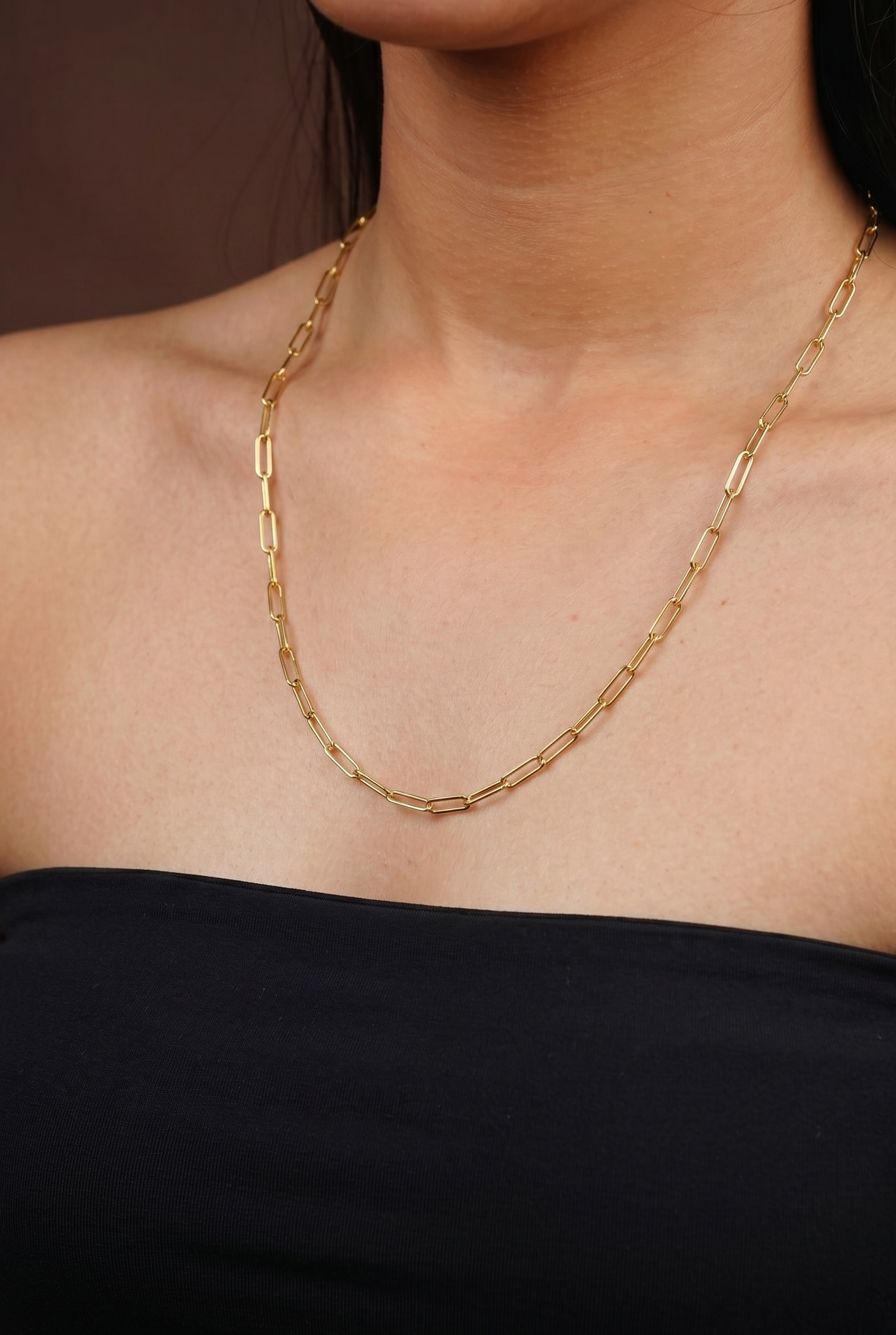Gold chain necklace on a person wearing a black top against a brown background