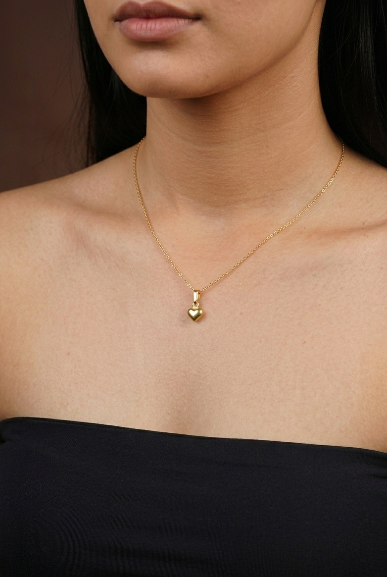 Gold necklace with a heart pendant worn by a person against a dark background